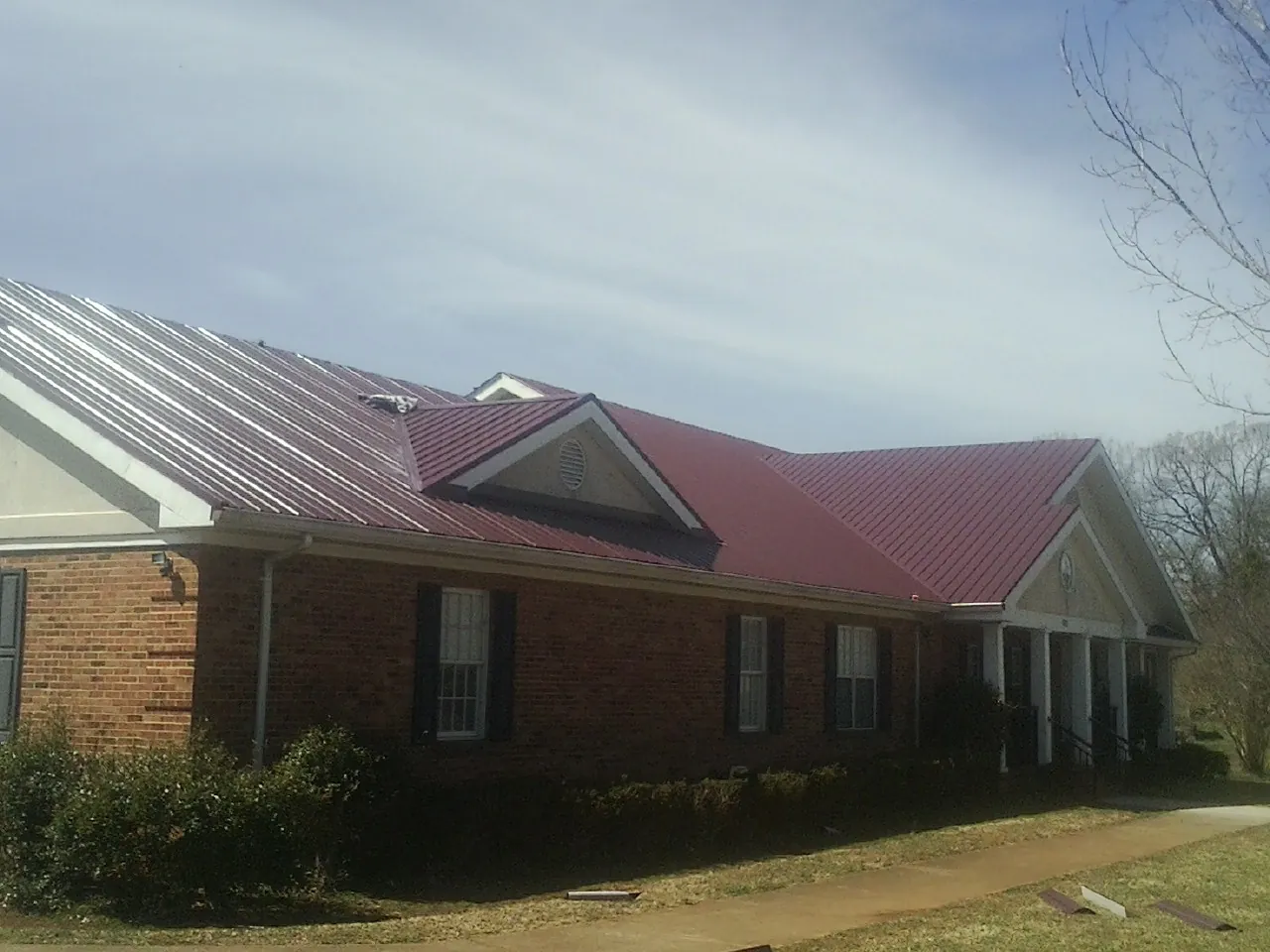 Red metal roof with gabled entries on a long brick building, from a Hail Damage Roof Repair job in Drewryville