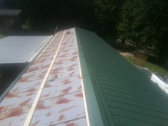 Old rusted panels beside newly installed green metal roofing — Wind Damage Roof Repair by Roofing Brothers in Drewryville