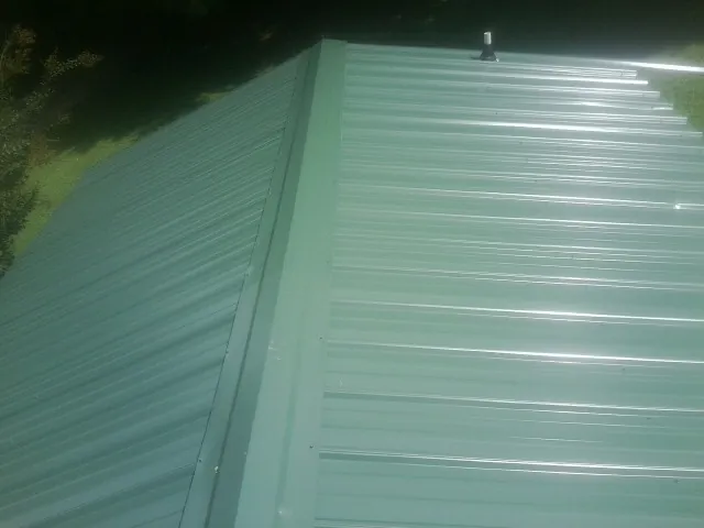 New green metal panels meeting at the ridge of a roof — Flat Roof Repair work by our crew in Drewryville