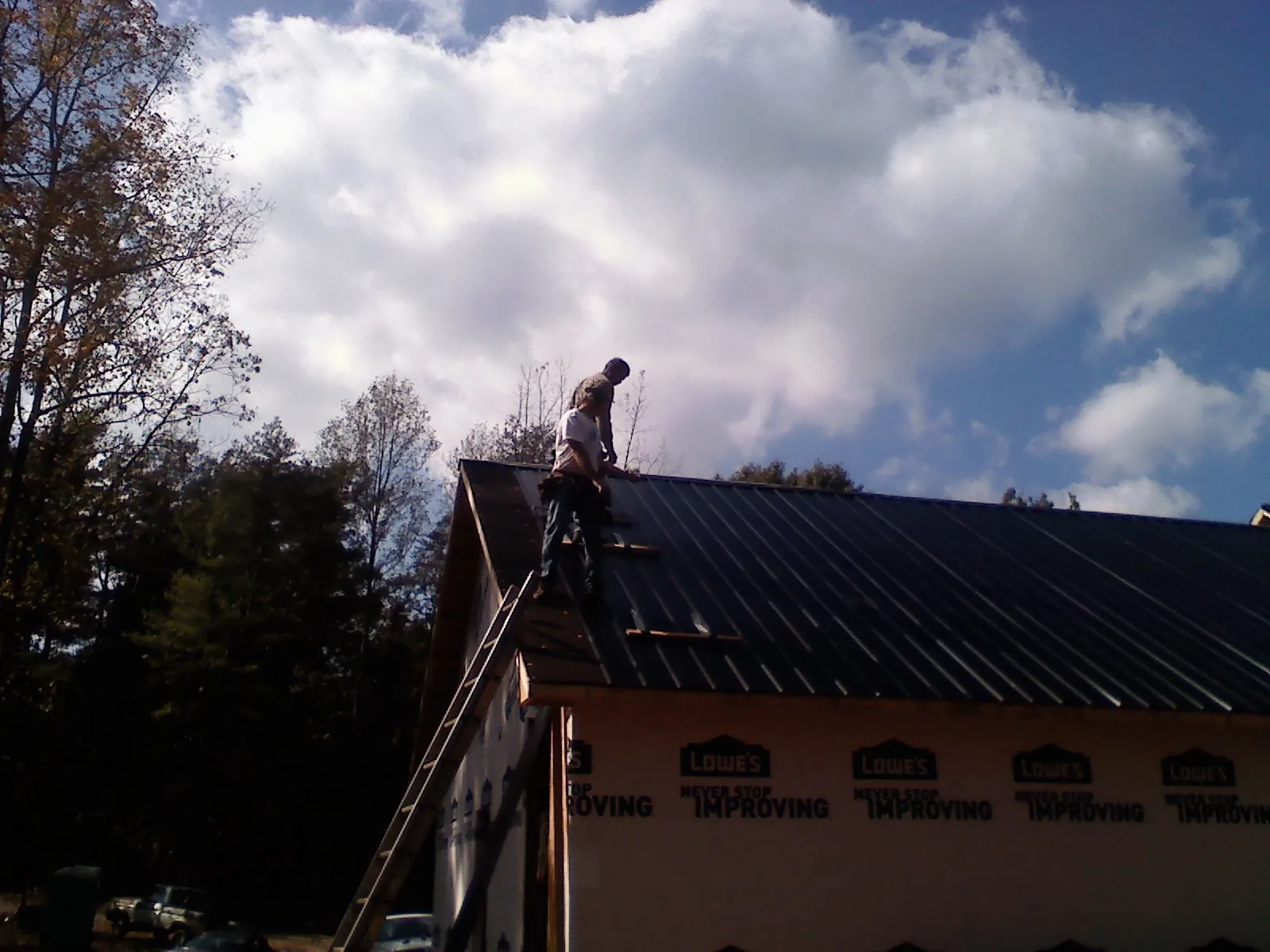 Roofer fastening dark metal panels high against a cloudy sky, from a Roof Inspection job in Drewryville
