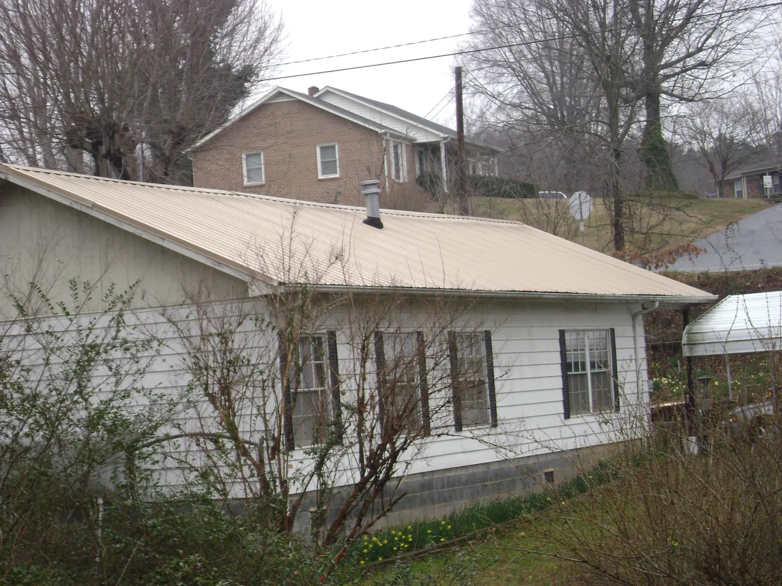 Tan metal roof on a white sided house set into a hillside — Commercial Roofing by Roofing Brothers in Drewryville