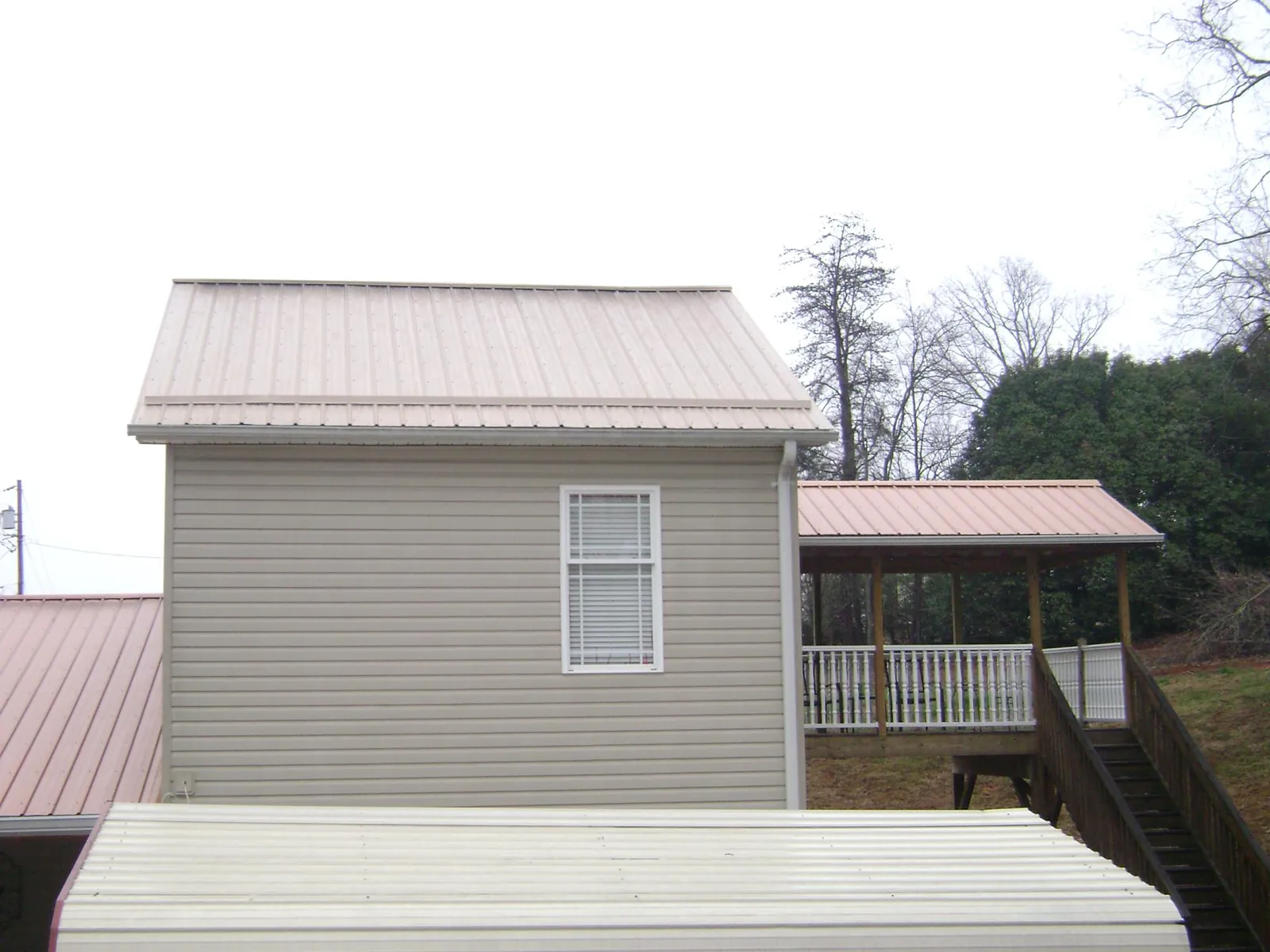 Tan metal roofs on a two story addition and attached porch, from a Roof Replacement job in Drewryville